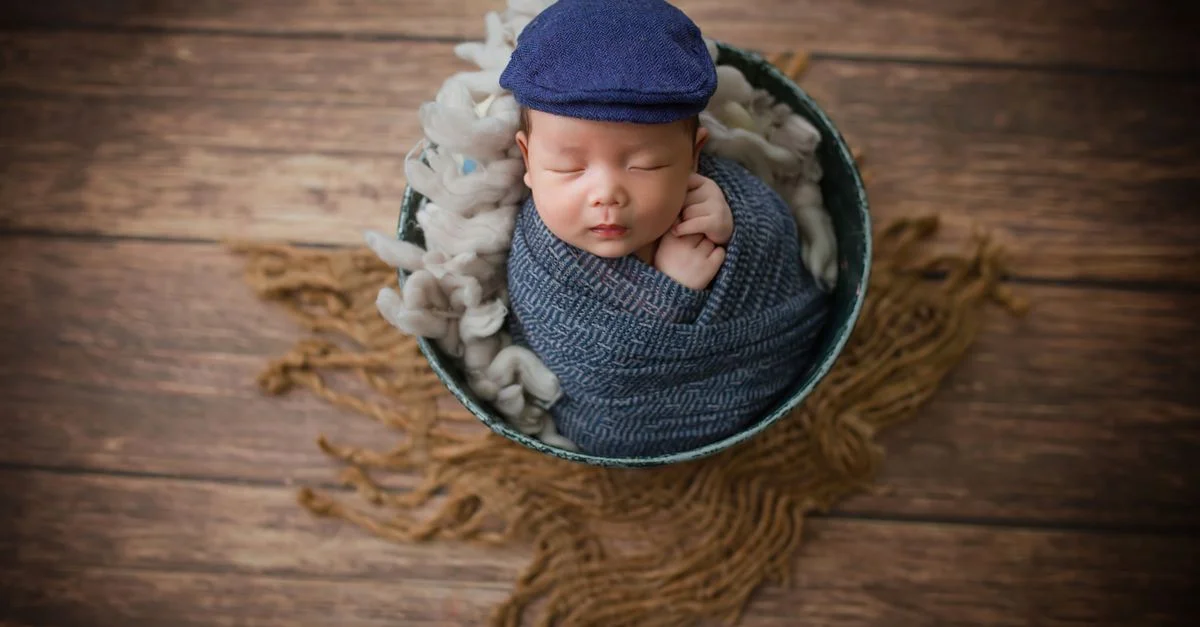 Bébé nouveau-né paisible dormant dans un bol avec un wrap bleu confortable et un chapeau.