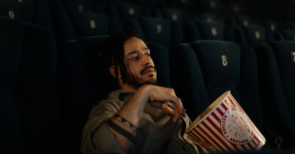 Homme assis seul dans une salle de cinéma, tenant un grand seau de popcorn.