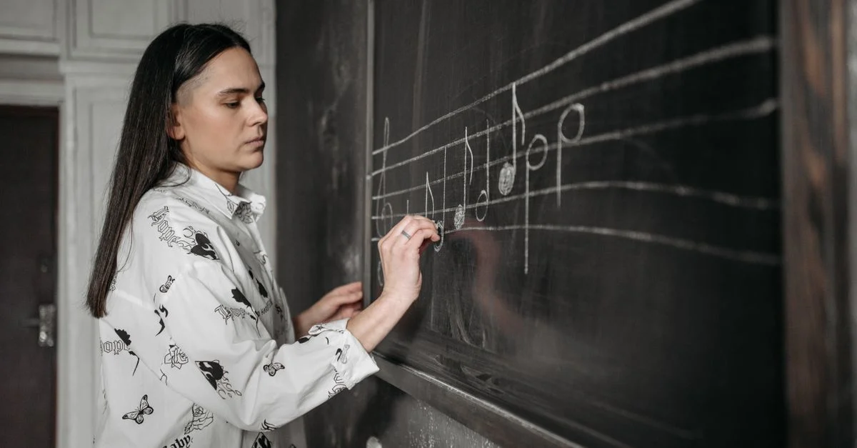 Une femme dessinant des notes musicales sur un tableau noir dans un cadre de classe.
